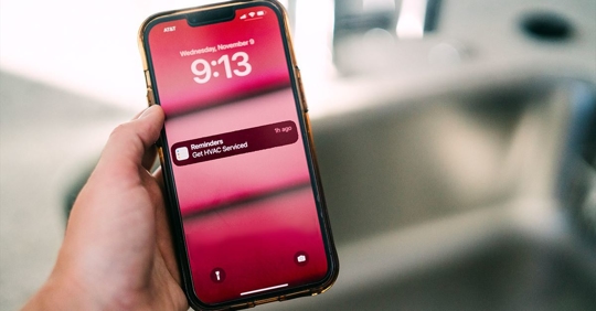 hand holding phone with HVAC reminder display on screen